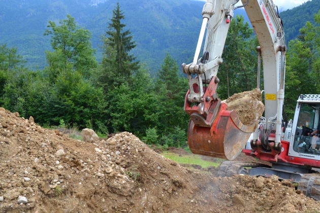 Bagger bei Aushubarbeiten mit Findling in Baggerlöffel