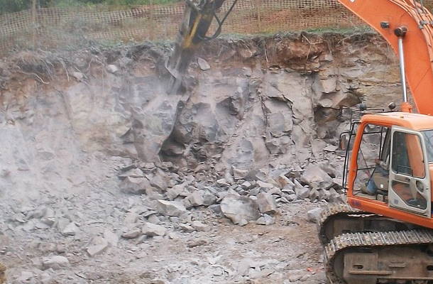 Bagger mit Hydraulikhammer bei Felsaushub für Baugrube